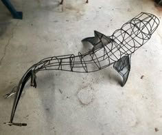 a metal fish sculpture sitting on top of a cement floor next to a wrench