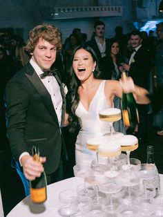 a man and woman standing next to each other in front of a table filled with champagne glasses