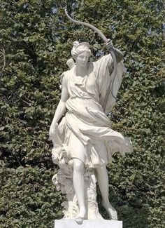 a statue of a woman holding a staff in front of some green bushes and trees