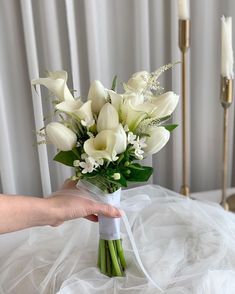 a bouquet of white flowers is being held by a person's hand on a bed