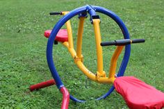 a small child's play set in the middle of a grassy area with red and blue seats