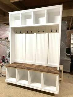 a white wooden bench sitting inside of a garage next to a wall mounted coat rack