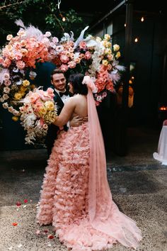 a bride and groom standing in front of a floral arch with pink flowers on it