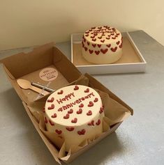 two birthday cakes sitting in boxes on top of a table with spoons and forks