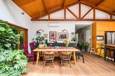 a dining room table surrounded by chairs and potted plants in front of an open kitchen