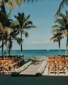 an outdoor ceremony set up on the beach with palm trees and white flowers in the foreground