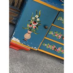 an old dresser with flowers painted on the side and drawers in different colors, including blue