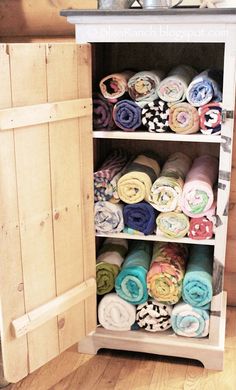 an open cabinet filled with lots of folded towels on top of wooden floor next to a wall