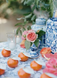 a table topped with blue and white vases filled with flowers next to oranges