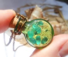 a hand holding a glass bottle with green sand inside it and a chain attached to it