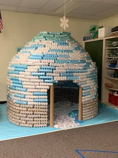 a building made out of water bottles in the middle of a room with blue and white flooring