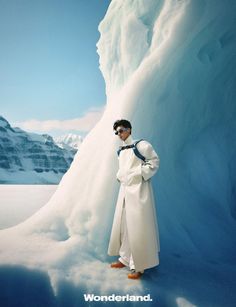 a man standing in front of an iceberg wearing sunglasses and a white coat with the word wonderland written on it