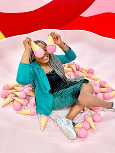 a woman sitting on top of a pile of doughnuts with pink and yellow cones