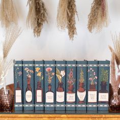 a row of books sitting on top of a wooden shelf next to dried flowers and plants