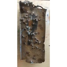 a piece of metal with holes and rivets hanging on the side of a wall