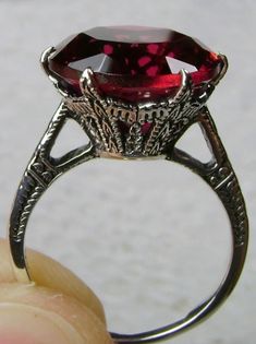 This is an Edwardian reproduction filigree ring in antiqued solid sterling silver. The round full cut high quality Simulated Red Ruby solitaire gemstone is 12mm in diameter. The inside of the band is marked 925 for sterling silver. Vintage Garnet Ruby Ring With Intricate Design, Ornate Ruby Ring With Intricate Design, Antique Ruby Filigree Ring With Gemstone, Ornate Ruby Ring With Filigree, Antique Ruby Ring With Intricate Design For Promise, Formal Silver Ruby Ring With Engraving, Garnet Rings With Intricate Design, Victorian Style Red Round Rings, Victorian Filigree Ring In Red As Gift