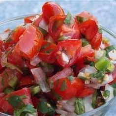 a glass bowl filled with chopped tomatoes and other veggies on top of a table