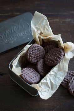 chocolate cookies in a tin on a wooden table with a wax paper wrapper next to it