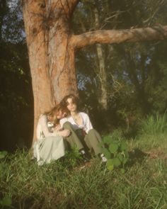 two people sitting next to each other in front of a large tree and grass area