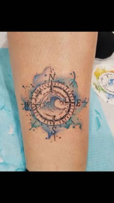 a tattoo on the leg of a person with a compass and wave in blue ink