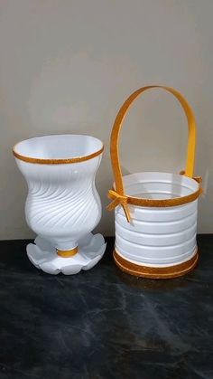 two white vases sitting next to each other on a black counter top with gold trim