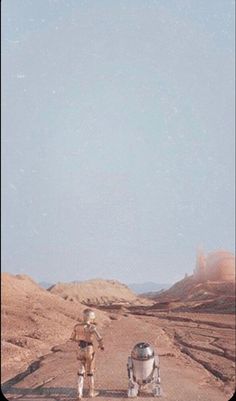 two people standing in the middle of a dirt road with an astronaut next to them