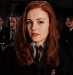 a woman with long red hair wearing a tie and looking at the camera while other people stand behind her