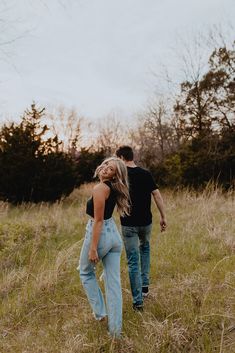 a man and woman are walking through the tall grass with their backs to each other