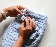 a woman is crocheting the edges of a blue blanket with her hands on it