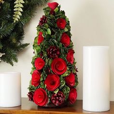 a christmas tree decorated with red roses and greenery next to two white candles on a table