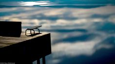 a bench sitting on top of a wooden pier next to the ocean under a cloudy sky