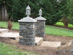 two stone pillars in the middle of a yard with steps leading up to them and trees in the background