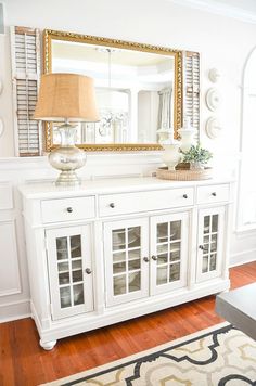 a living room with white furniture and a large mirror on the wall over it's sideboard