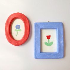 two small frames with flowers on them are next to each other, one is red and the other is blue