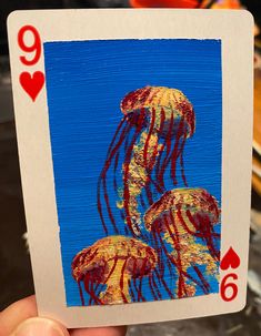 a hand holding up a playing card with two jellyfishs on it