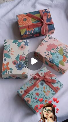 four wrapped gift boxes sitting on top of a white sheet with flowers and hearts around them