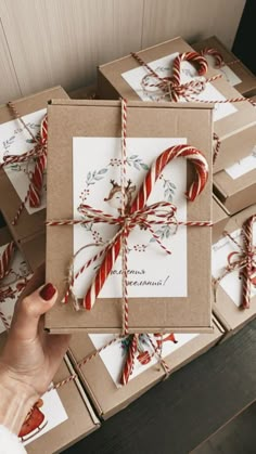 a person holding a candy cane in front of several boxes with cards on them and wrapped in twine