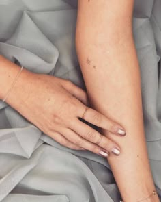 a woman's arm and hand on top of a gray sheeted bed spread