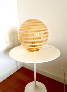 a table with a lamp on top of it in front of a white wall and wooden floor