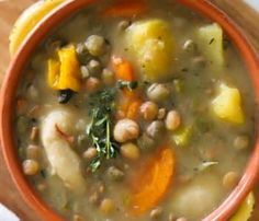 a bowl of soup with potatoes, carrots and other vegetables on a wooden table