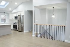 an empty kitchen with stainless steel appliances and white walls, hardwood floors, and skylights