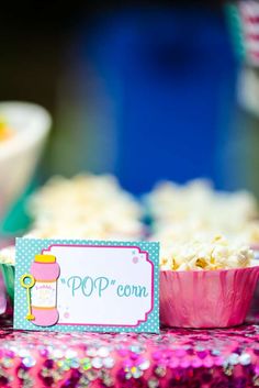 a table topped with pink cups filled with popcorn and a sign that says pop corn