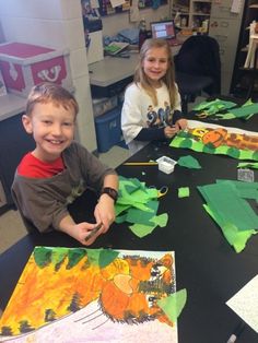 two young children sitting at a table making art work with paper and construction supplies on it