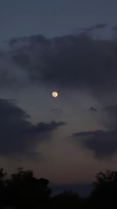 the moon is seen through some clouds in the night sky, with trees silhouetted against it