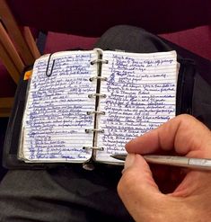 a person holding a cell phone and writing on a notebook