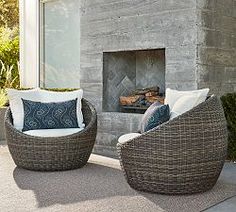 two wicker chairs sitting in front of a fire place with pillows on the cushions