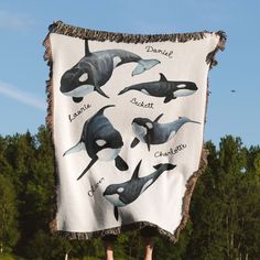 an orca whale blanket hanging on a pole in front of some trees and grass