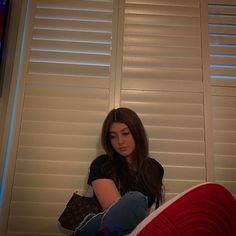 a young woman sitting on the floor in front of a window with white shutters