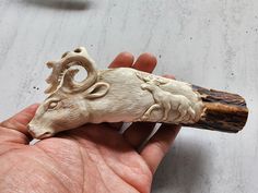 a hand holding a carved animal head on top of a piece of wood