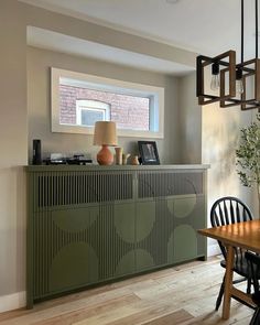 a dining room table with chairs and a vase on top of the buffet cabinet, in front of a window